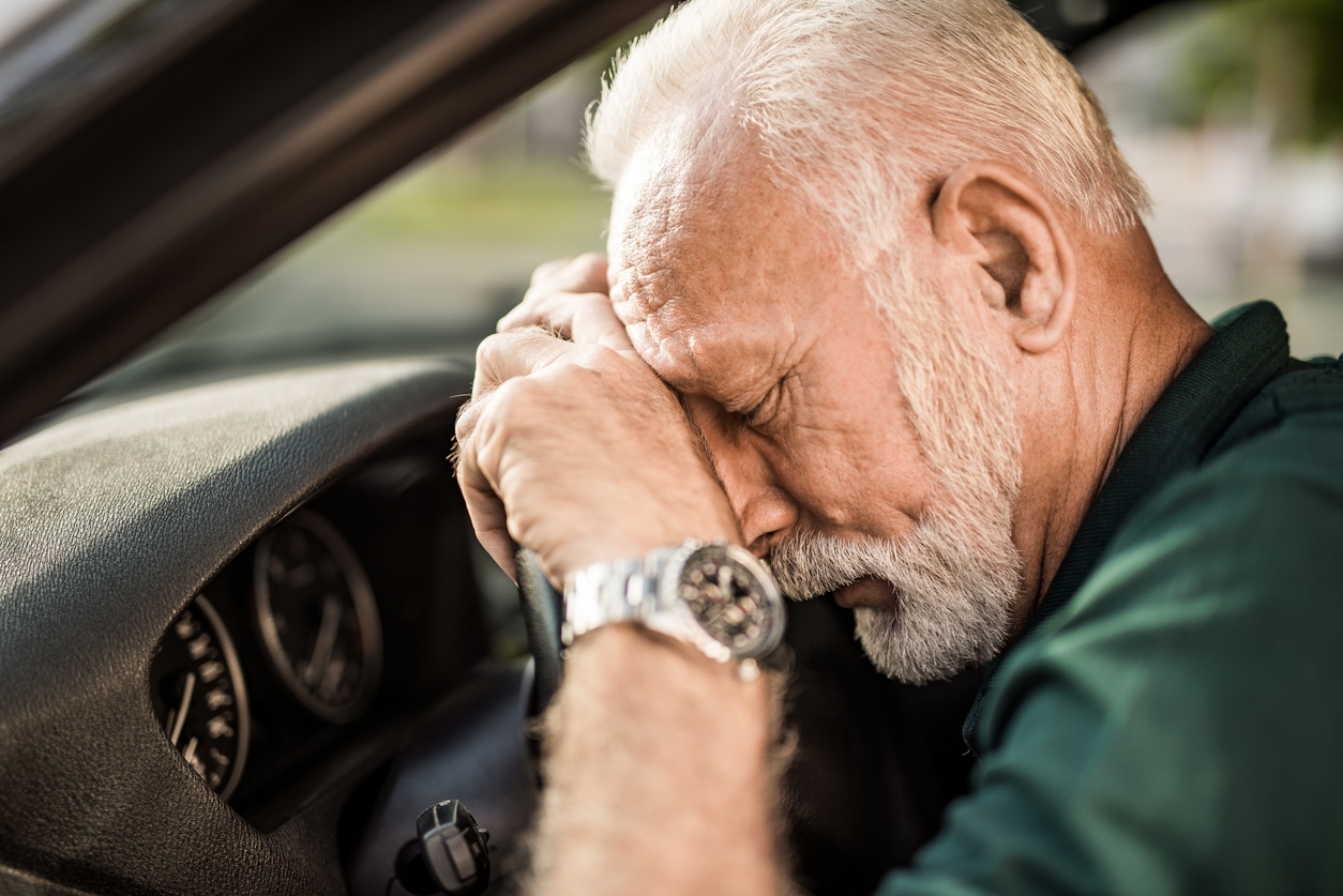 Senior man leaning on a steering wheel after a car accident.